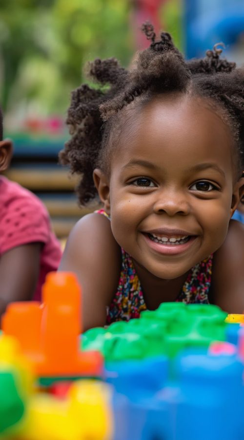 Three African American children with bright smiles playing with multicolored plastic building blocks outside